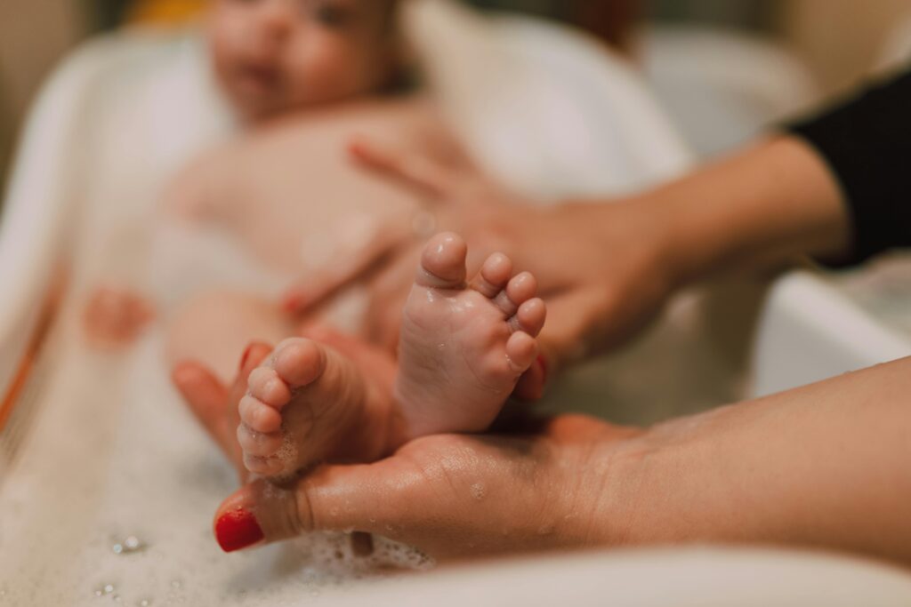 a newborn's feet stick out of the baby bathtub as its mother bathes them. This photo evokes a strong emotion of joy which is one way to use website design for social change.